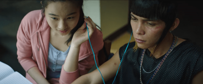 Lin, una adolescente china, compartiendo audifonos con Ulises, un joven moreno. Ella tiene expresión alegre y Ulises seria